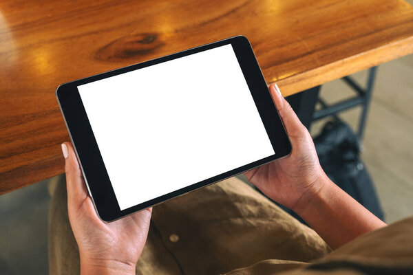 Mockup image of a woman sitting and holding black tablet pc with blank white desktop screen horizontally