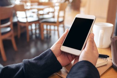 El ele tutuşmanın ve beyaz bir cep telefonu kullanmanın görüntüsü. Kafedeki ahşap masa üzerinde defter ve kahve fincanı olan boş bir ekran.