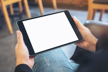 Kafede otururken elinde boş beyaz ekranlı siyah tablet tutan bir kadının görüntüsü.
