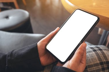 Kafedeki boş beyaz ekranlı siyah cep telefonunu tutan ellerin görüntüsü