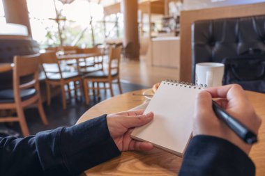 Kafe 'deki boş bir defterin üzerine el ele tutuşup yazmanın yakın plan resmi.