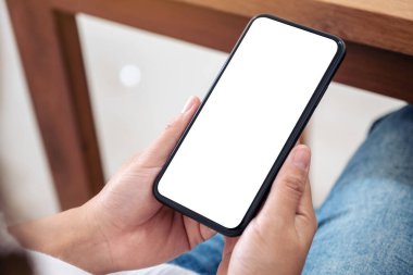 Otururken boş beyaz ekran ile siyah cep telefonu tutan ellerin görüntüsü 