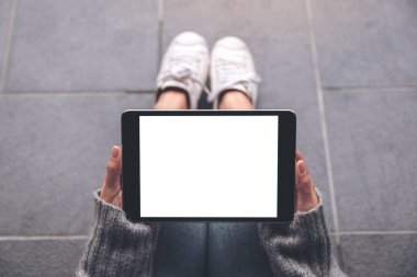 Üst görünümde, yerde otururken beyaz masaüstü ekranlı ve siyah tablet tableti kullanan kadınların ellerinin görüntüsü var 