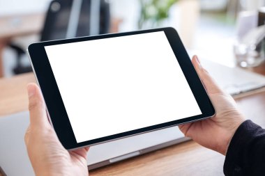 Ofisteki ahşap masadaki defter ile birlikte boş beyaz masaüstü ekranı olan siyah tablet bilgisayarın el ele tutuşunu ve kullanımını görüntüle