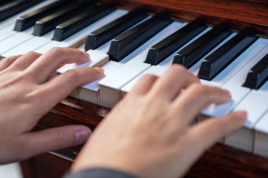 Kapalı çekimde, klasik ahşap bir piyanoyu çalan ellerin görüntüsü