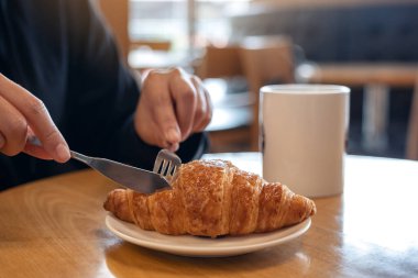 Ellerin kahvaltıda çatalla kruvasan keserken, kahve fincanını ahşap masada keserken yakın plan görüntüsü. 