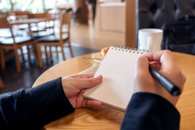 Kafe 'deki masada elinde kruvasanla elinde boş bir defterle yazan bir kadının yakın plan fotoğrafı.