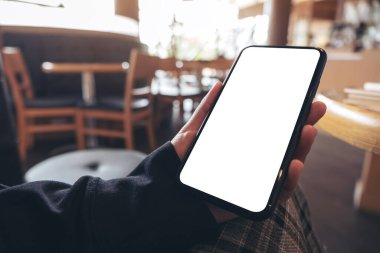 Kafedeki boş beyaz ekranlı siyah cep telefonunu tutan ellerin görüntüsü