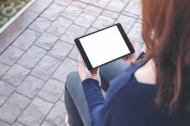 Açık havada otururken elinde beyaz ekranlı siyah tablet tutan bir kadının görüntüsü.