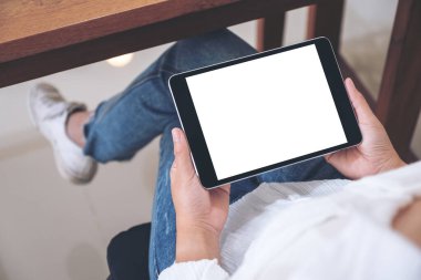 Kafede otururken elinde boş beyaz ekranlı siyah tablet tutan bir kadının görüntüsü.