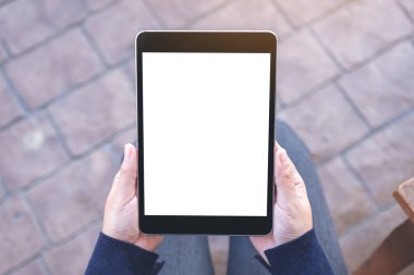 Üst görünümde, açık havada otururken elinde siyah tablet olan beyaz ekranlı bir kadının görüntüsü var.