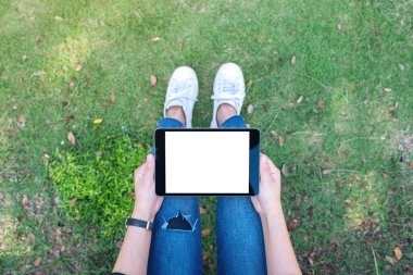 Açık havada otururken boş beyaz masaüstü ekran ile siyah tablet tableti tutan ve kullanan bir kadının en üst görünüm görüntüsü