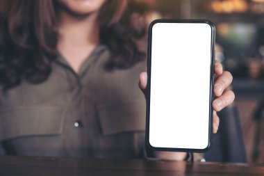 Modern kafedeki masada elinde siyah bir cep telefonu tutan ve gösteren beyaz ekranlı bir kadının görüntüsü.