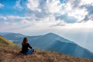 Bir kadın oturuyor ve akşamları dağ manzaralı gün batımını seyrediyor.