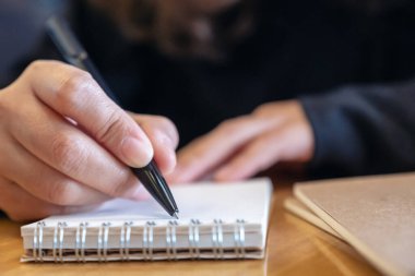 Tahta masaya boş defter yazan bir kadının yakın plan resmi.