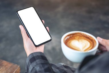 Kafede kahve içerken siyah cep telefonunu boş ekran ile tutan bir elin görüntüsü.