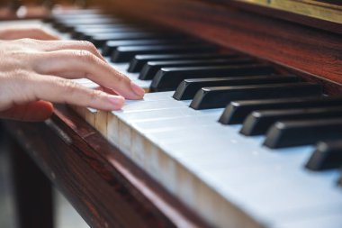 Kapalı çekimde, klasik ahşap bir piyanoyu çalan ellerin görüntüsü