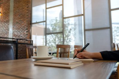 Kafe 'de kahve fincanı ile boş bir deftere el yazısının yakın plan resmi.