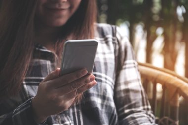 Güzel bir Asyalı kadının açık havada otururken akıllı telefonu tutarken ve ona bakarken yakın plan görüntüsü.