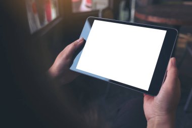 Eski ahşap kafede boş beyaz masaüstü ekranı olan siyah tableti tutan ellerin görüntüsü