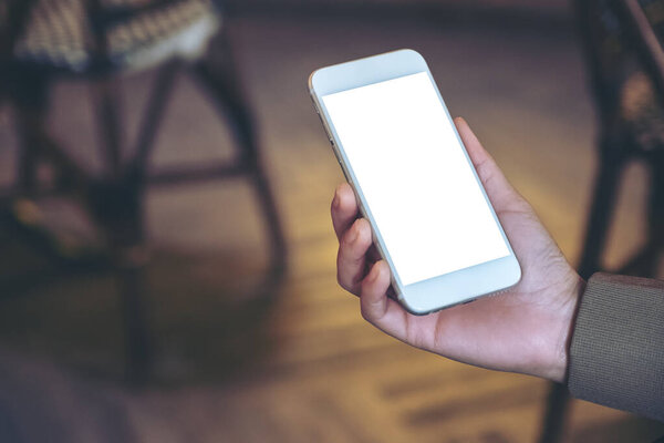 Mockup image of a hand holding white mobile phone with blank desktop screen with blur background