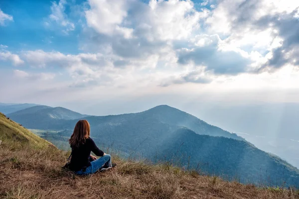 Bir kadın oturuyor ve akşamları dağ manzaralı gün batımını seyrediyor.