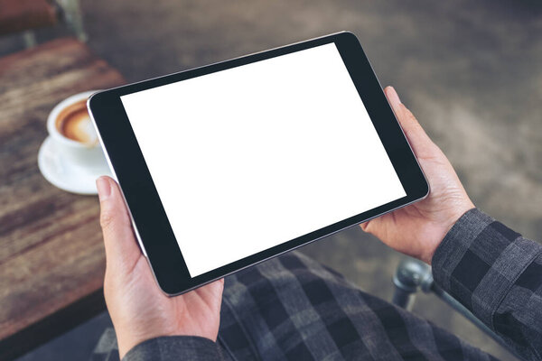 Mockup image of woman's hands holding black tablet pc with blank screen with coffee cup on wooden table in cafe