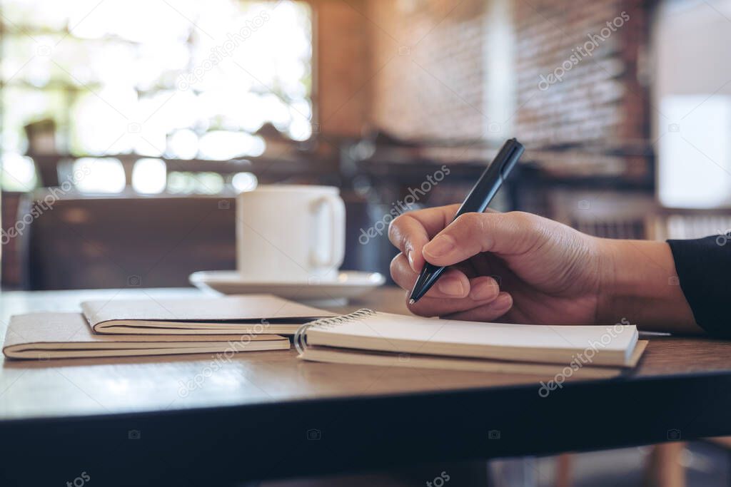 Closeup image of a hand writing on blank notebook with coffee cup on table in cafe
