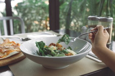 Restorandaki yemek masasında pizza yemek için Sezar salatası kepçesinde çatal kullanan bir el. 