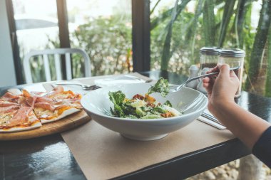 Restorandaki yemek masasında pizza yemek için Sezar salatası kepçesinde çatal kullanan bir el. 