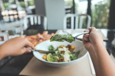 Restorandaki yemek masasında pizza yemek için Sezar salatası kepçesinde çatal kullanan bir el. 