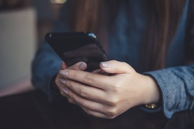 Masadaki akıllı telefonu tutan, kullanan ve ona bakan bir kadının yakın plan görüntüsü.