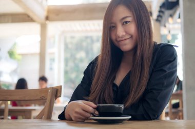 Kafede rahatça kahve içen Asyalı güzel bir kadının görüntüsü.