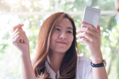 Güzel bir Asyalı kadının elinde tuttuğu, mutlu hissederek akıllı telefona baktığı yakın plan görüntüsü.