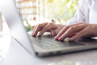 Bilgisayardaki klavyede çalışan ve yazı yazan ellerin yakın plan resmi.