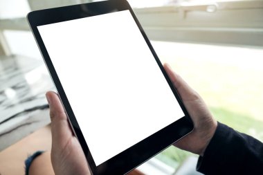 Kafede boş beyaz masaüstü ekranı olan siyah tableti tutan ellerin görüntüsü