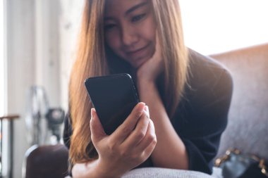 Güzel bir Asyalı kadının elinde tuttuğu, mutlu hissederek akıllı telefona baktığı yakın plan görüntüsü.