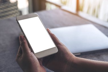Masada boş masaüstü ekranı ve dizüstü bilgisayarı olan beyaz cep telefonu tutan ellerin görüntüsü