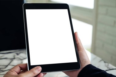 Masada boş beyaz masaüstü ekranı olan siyah tableti tutan ellerin görüntüsü 