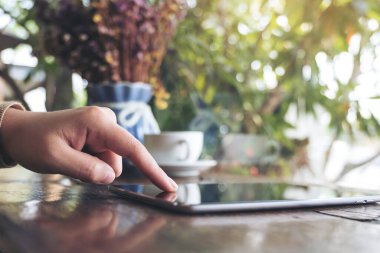 Kafe 'deki ahşap masanın üzerindeki tablet bilgisayarı işaret eden, dokunan ve kullanan bir kadının yakın plan görüntüsü.