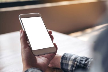 Kafede boş masaüstü ekranı olan beyaz cep telefonu tutan bir elin görüntüsü