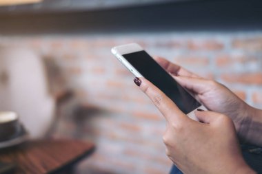 Kafede arka planda bulanık bir cep telefonu tutan bir kadının yakın plan fotoğrafı.