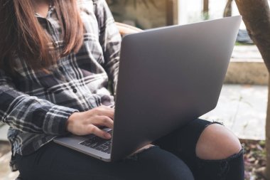 Dışarıda otururken dizüstü bilgisayar kullanan ve yazan bir kadın. 