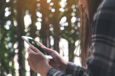 Elinde tutan, kullanan ve akıllı telefona bakan bir kadının görüntüsü bulanık yeşil doğalı.