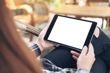 Kafede arka planı bulanık beyaz ekranlı siyah tabletli bir kadının görüntüsü.