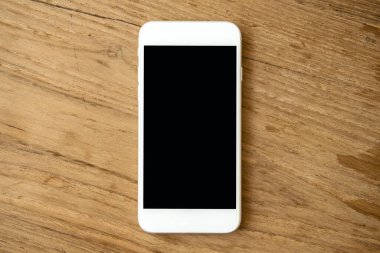 Eski ahşap masa arka planında boş siyah ekranlı beyaz cep telefonunun görüntüsü