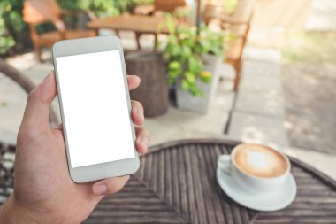 Açık arka planı bulanık olan kahve dükkanında beyaz cep telefonu ve boş masaüstü ekran görüntüsü.