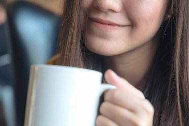 Güzel bir Asyalı kadının elinde beyaz bir fincan kahveyle kafede mutlu olduğu yakın plan görüntüsü.