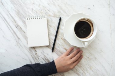 Bir elin en üstteki görüntüsü boş beyaz bir deftere kahve fincanı ile yazılacak.