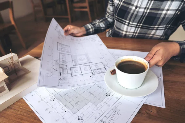 An architect working on an architecture model with shop drawing paper while drinking coffee